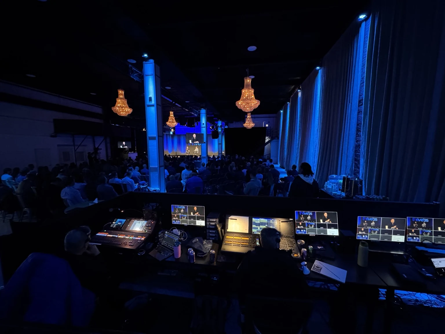 Thrive ’25: broadcast production monitors facing the live audience and blue-lit stage